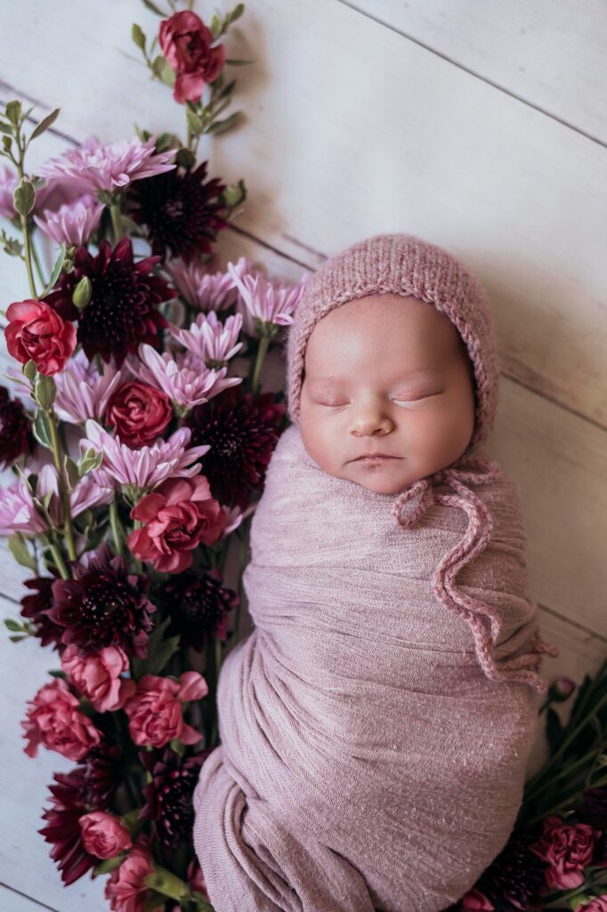 Boho baby girl in pink bonnet surrounded by flowers – newborn photographer in Sacramento CA